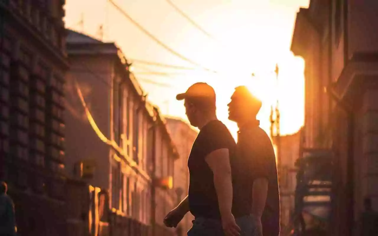 How to support someone with schizoaffective disorder. Two male friends walk along an urban street at sunset.