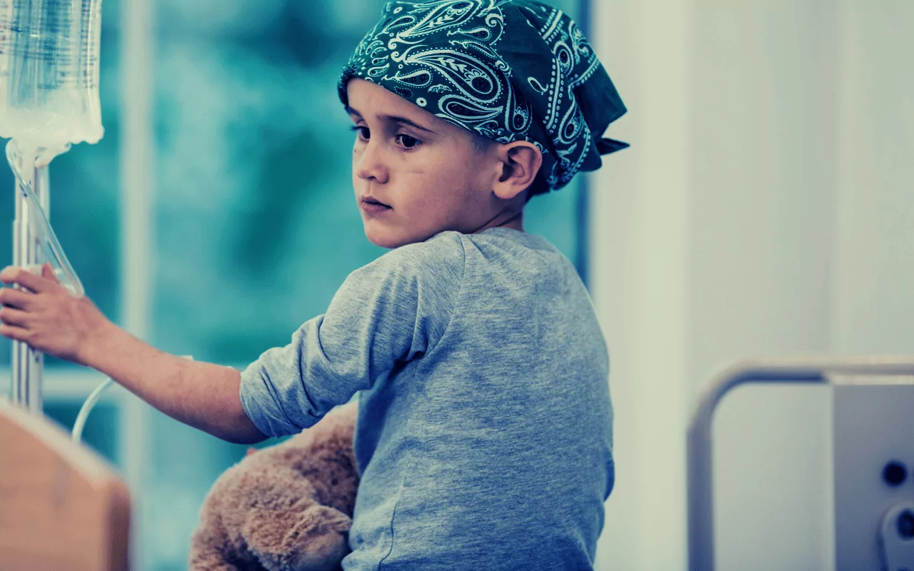 Boy with Wilms tumor cancer wearing a green head scarf and holding an IV pole.
