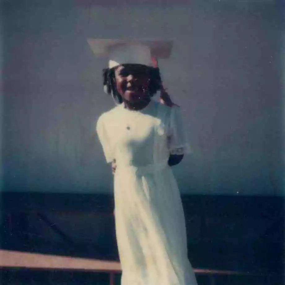 Alisa graduating from elementary school, wearing a white dress and graduation cap.
