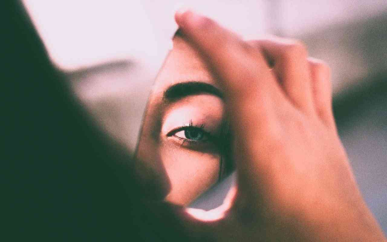 Overcoming body dysmorphia and feeling ugly. How to get comfortable in your own skin. Image of a woman's eye reflected in a piece o f broken mirror.