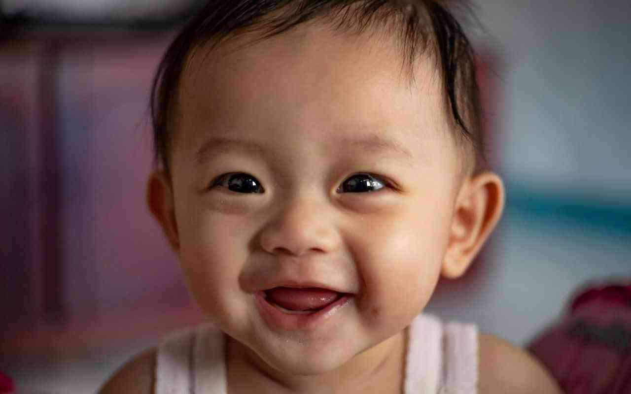 Tips for choosing and caring for baby clothes. Image shows a smiling baby of Asian heritage.