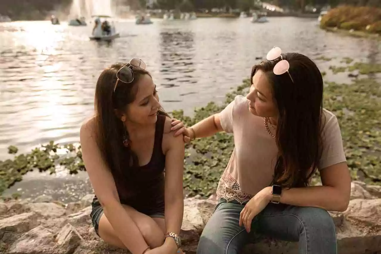 Supporting a loved one recovering from psychosis. A woman placing her hand on another woman's shoulder as they sit by a lake.