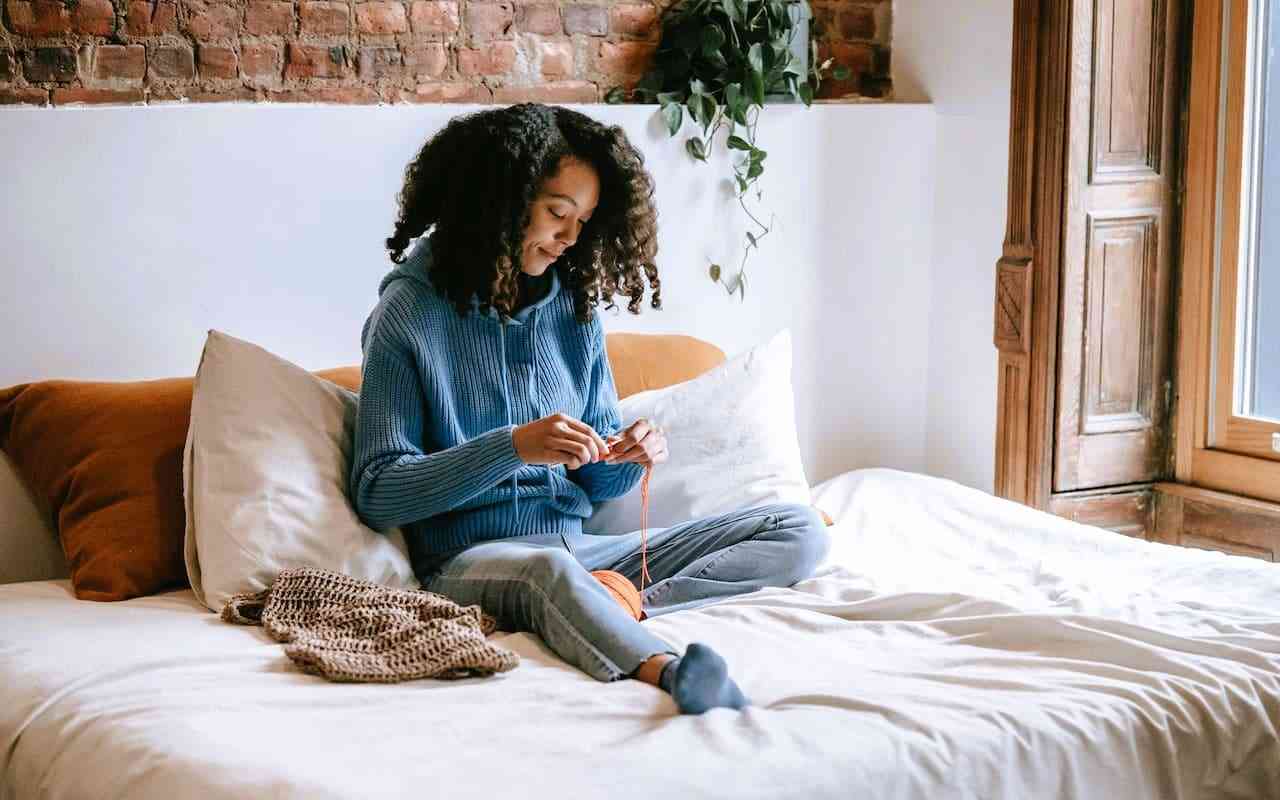 Purposeful yet restful self-care activities for people with chronic illness. Woman doing crochet in bed.