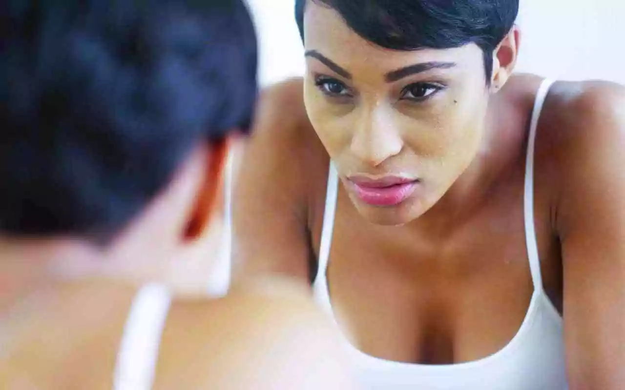 Stop self-abandonment after abuse. Woman looking in the mirror with determination.