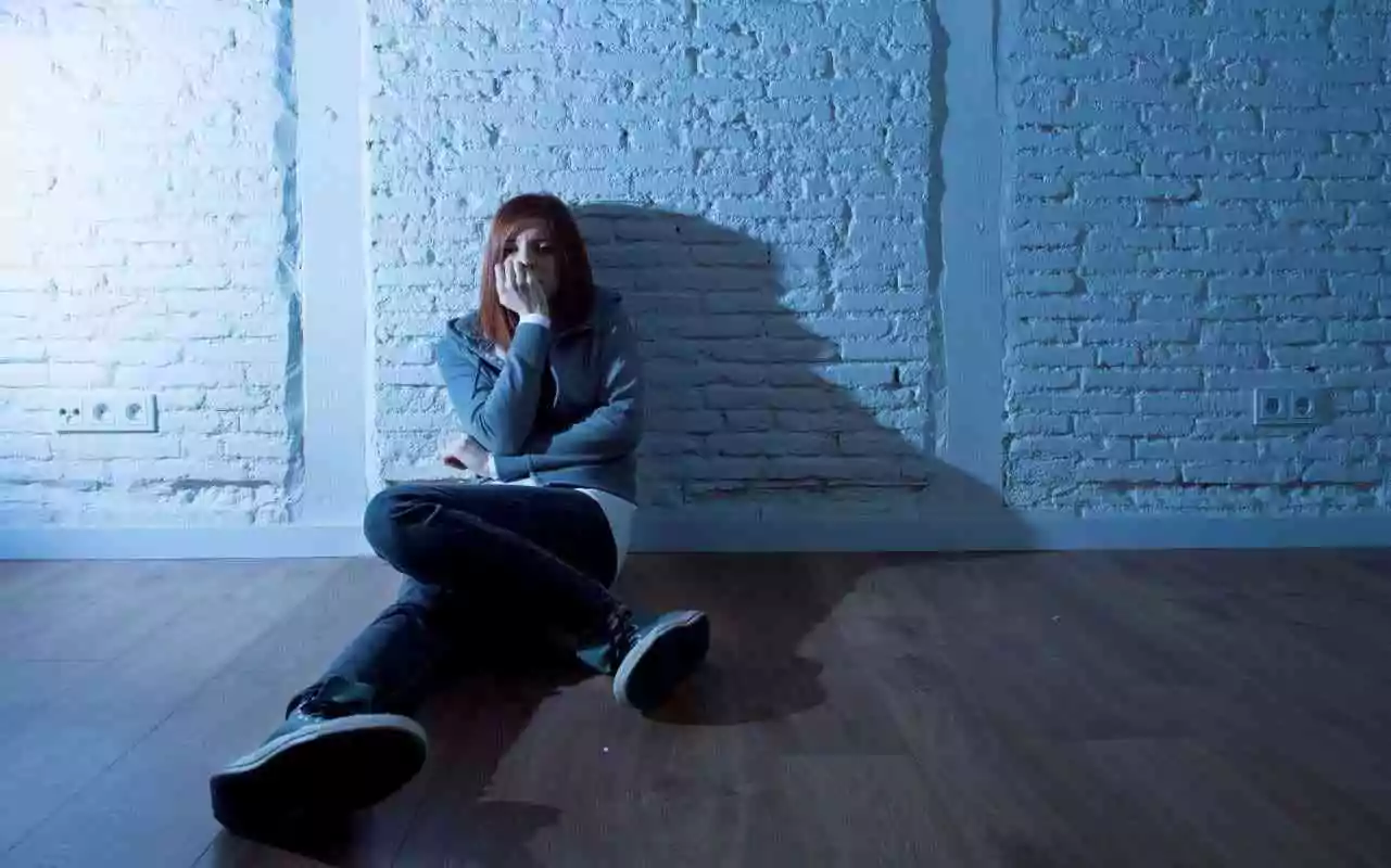 Teen with bipolar disorder sitting in dark room feeling sad.
