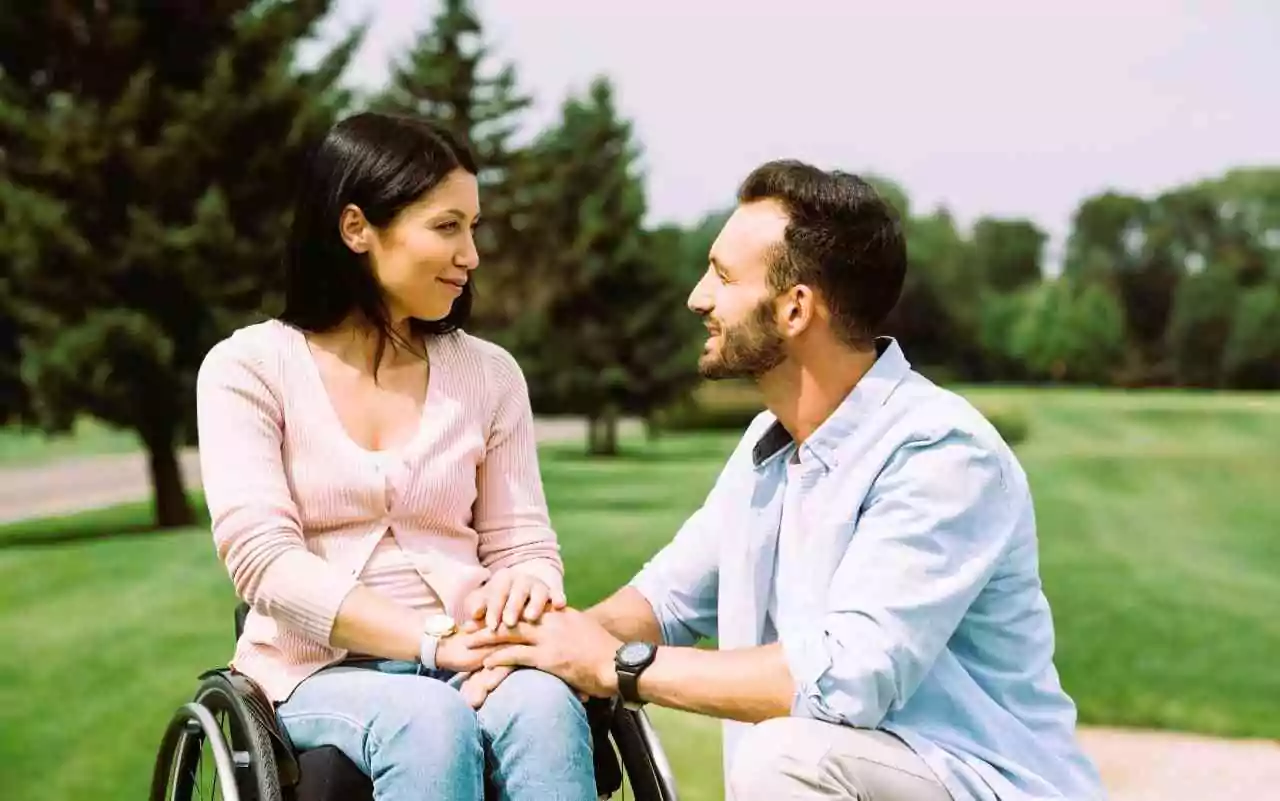 Dating with a disability. Woman in wheelchair holding hands with a man kneeling beside her.