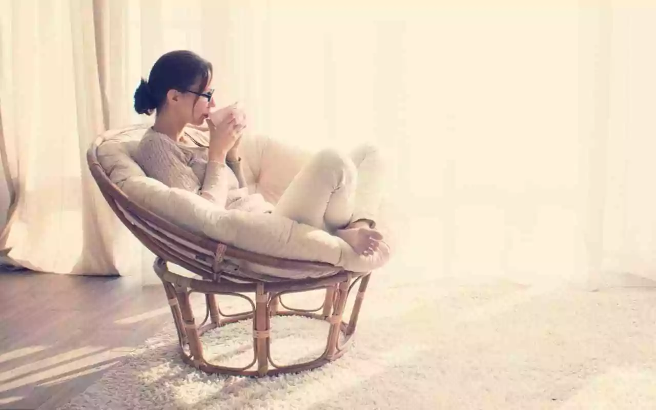 Anxiety management techniques. Woman relaxing in a papasan chair drinking coffee.