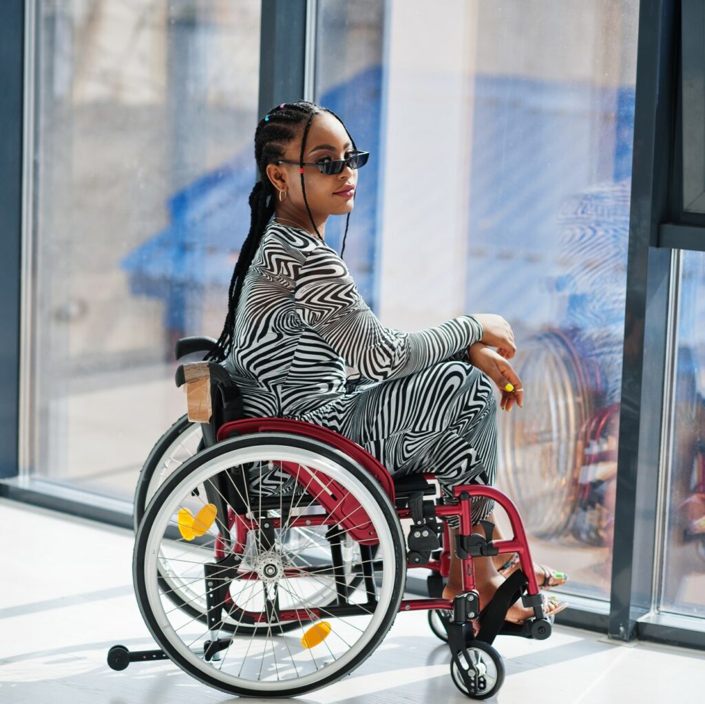 Black woman with long braids and zebra print dress sitting in a red manual wheelchair.