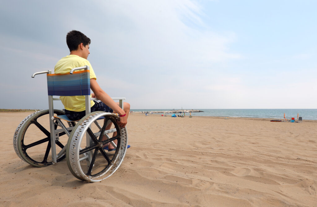 Boy in beach wheelchair by the ocean.