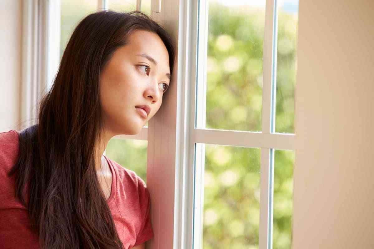 Addressing mental illness stigma in Asian cultures. Sad East Asian woman looking out window.