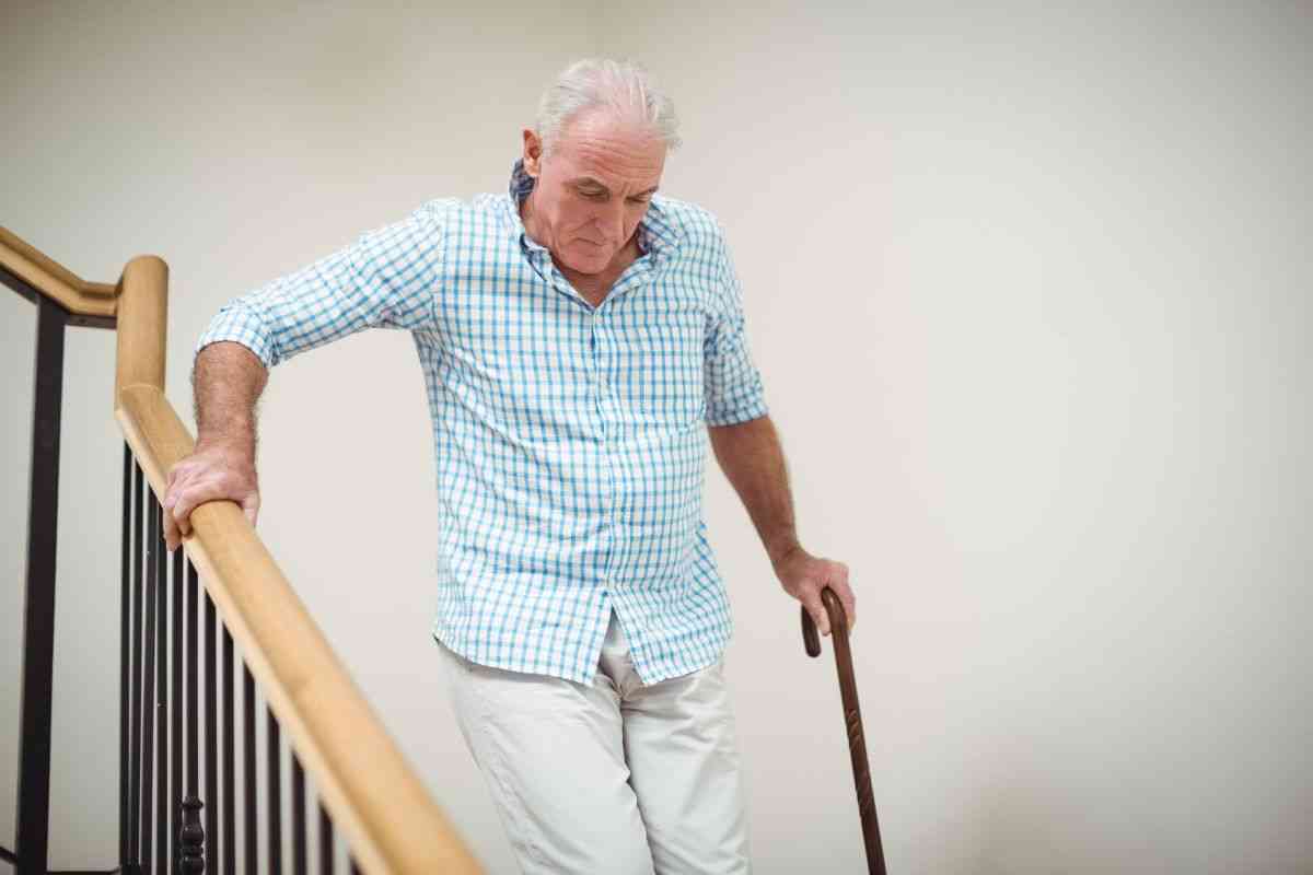 Senior man with disability and cane struggling to use stairs.