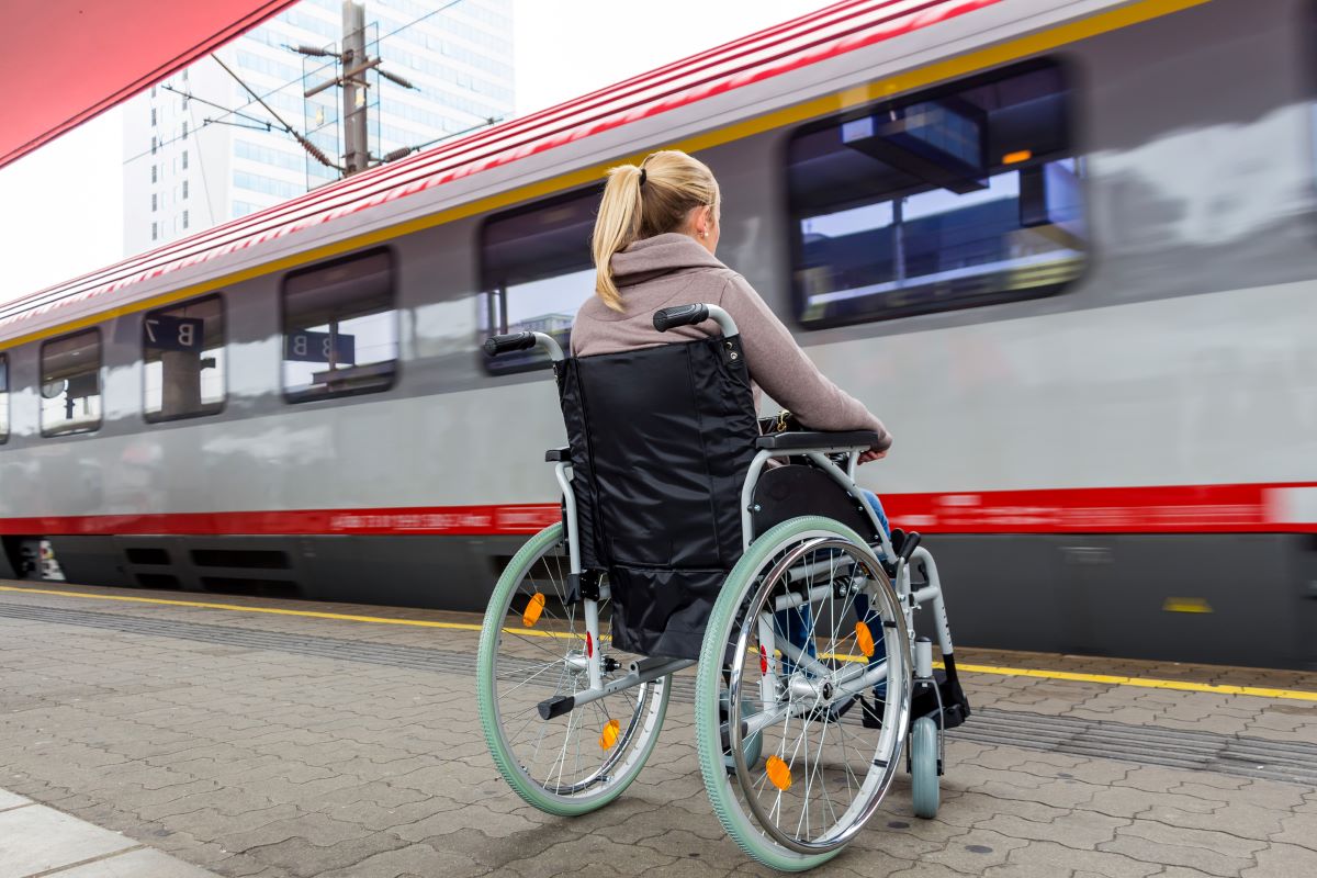 Tips for taking public transit alone with a disability. Woman in wheelchair waiting to board train at station.
