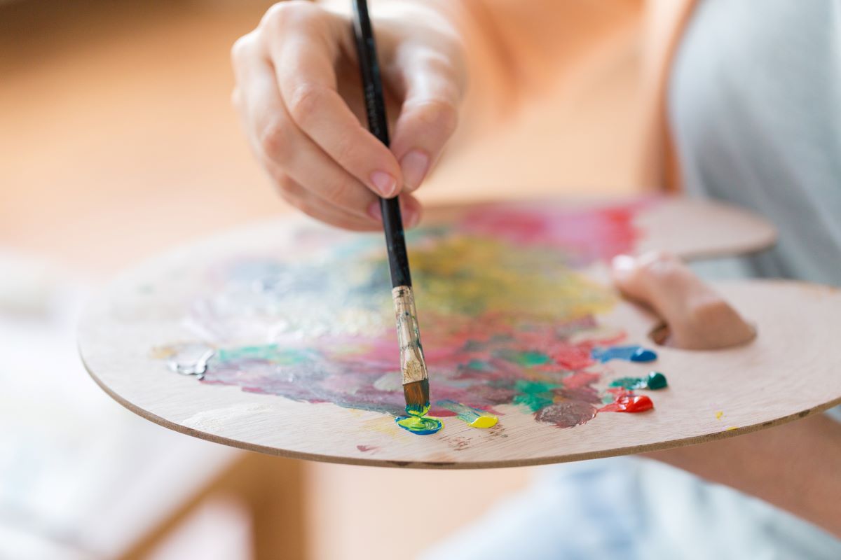 Person with a palette and paintbrush doing art therapy.