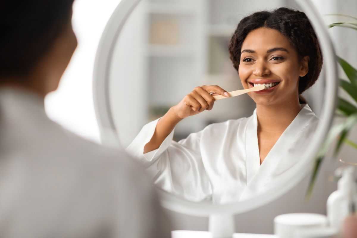 Tips for healthy teeth and gums. Woman brushing her teeth in the mirror.