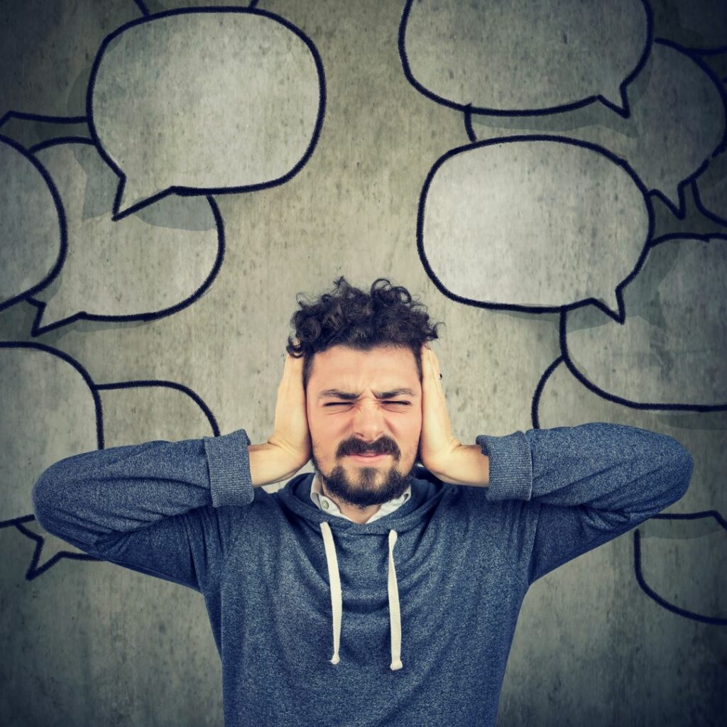 What autism feels like in loud environments. Man covering his ears with word bubbles behind him.